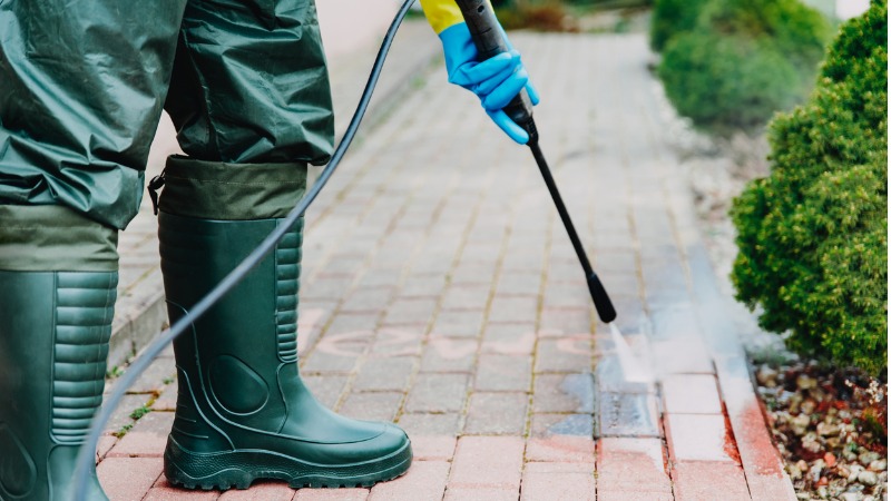 persoon draagt waterdichte kleding en regenlaarzen tijdens het gebruik van hogedrukreiniger